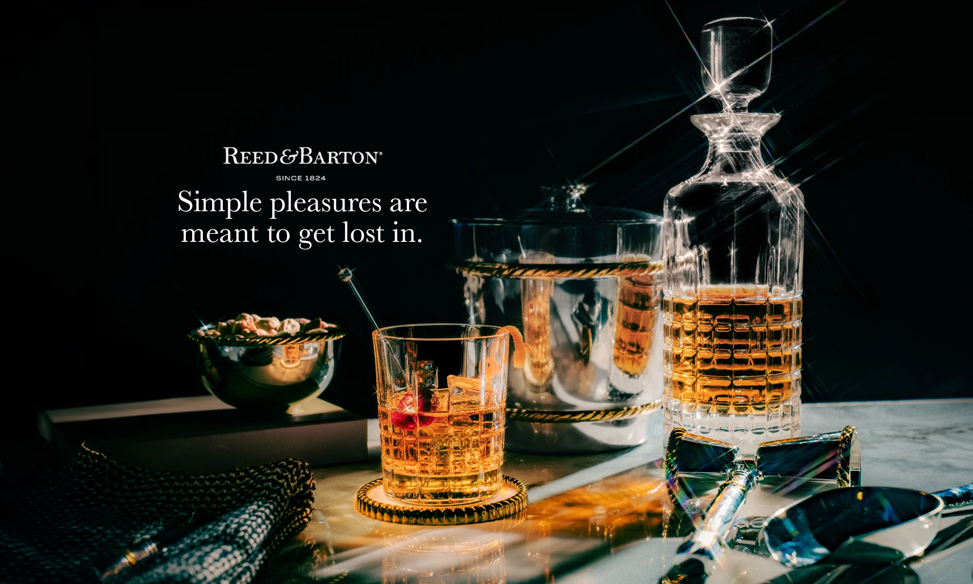 Glass of whiskey with a decanter on a table, featuring Reed & Barton branding.